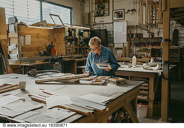 Senior female carpenter holding frame while working at workshop