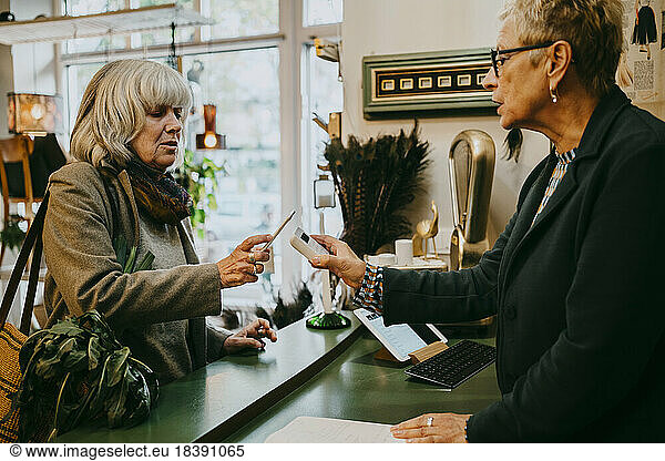 Senior female customer talking to owner while doing online payment at store