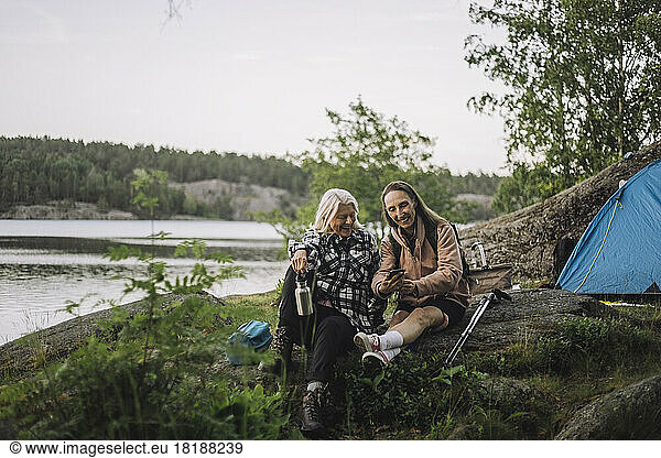 Senior female friends sharing smart phone while sitting on rock during camping
