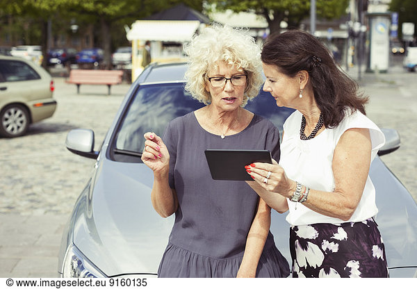 Senior female friends using digital tablet against car on street