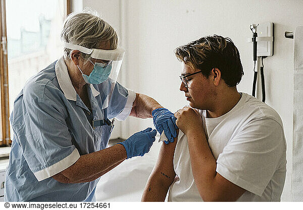 Senior female healthcare worker giving vaccine to young male patient during COVID-19