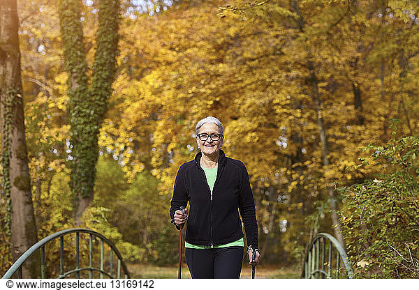 Senior female nordic walker crossing footbridge in autumn park