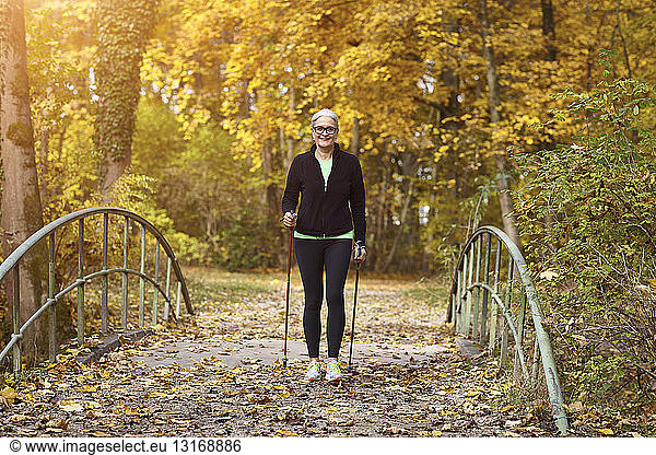 Senior female nordic walker crossing over footbridge in autumn park