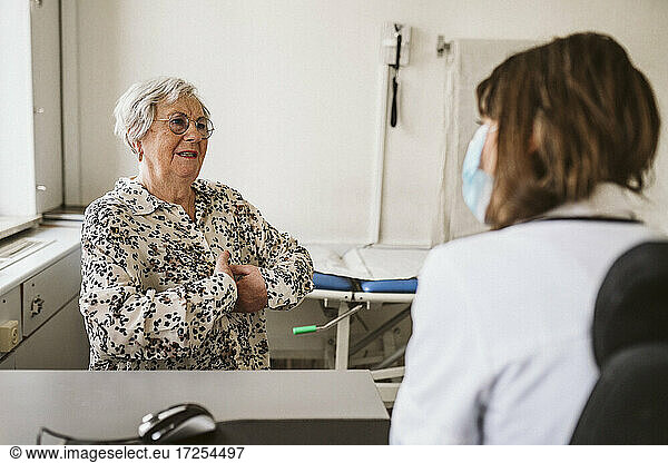 Senior female patient discussing with healthcare worker while consulting during COVID-19