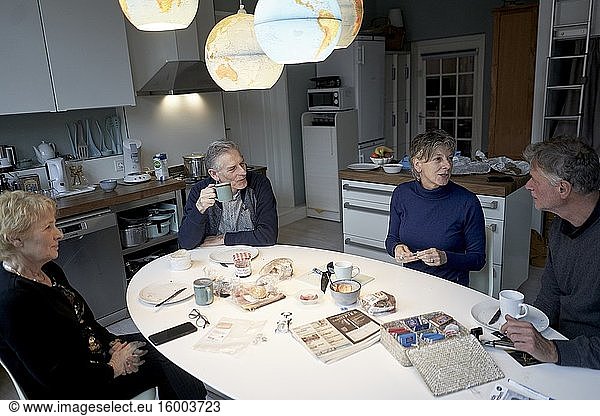 Senior friends eating breakfast together in kitchen under world globes