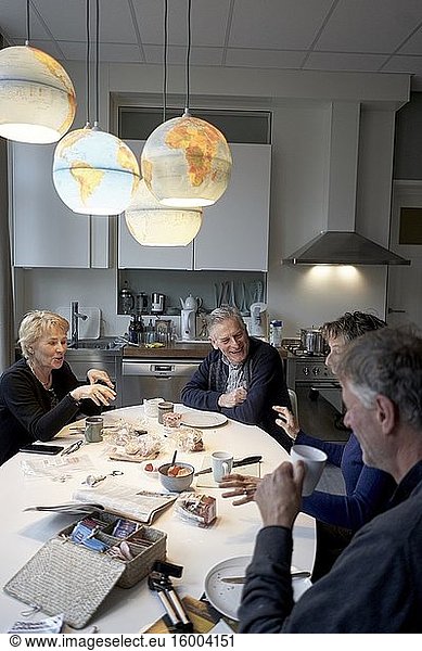 Senior friends eating breakfast together in kitchen under world globes