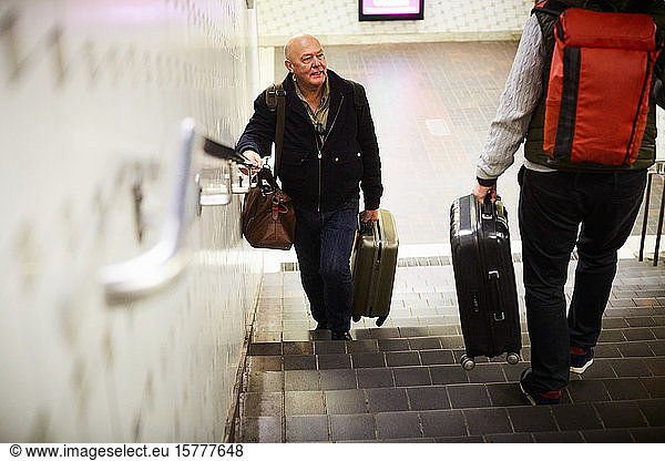Senior gay couple with luggage on staircase in subway