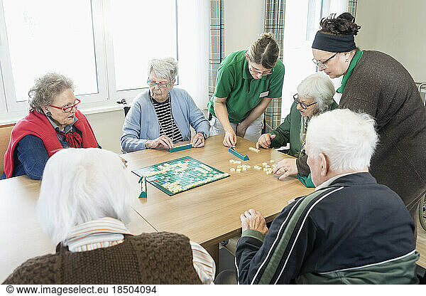Senior inhabitants playing board game with nurse in rest home