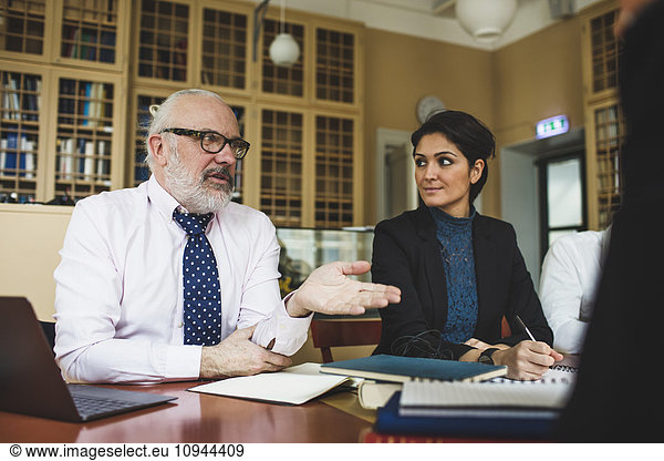 Senior lawyer discussing with coworkers during meeting in library