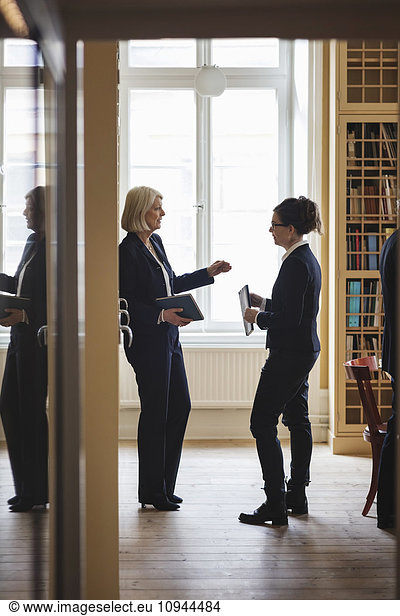 Senior lawyer discussing with female coworker while standing in library seen from doorway