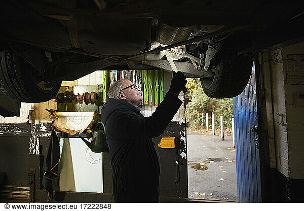 Senior male auto mechanic examining car in workshop