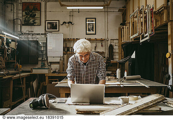 Senior male carpenter working on laptop at repair shop