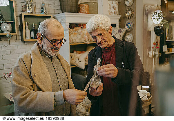 Senior male customer checking price tag of glass figurine held by owner at store