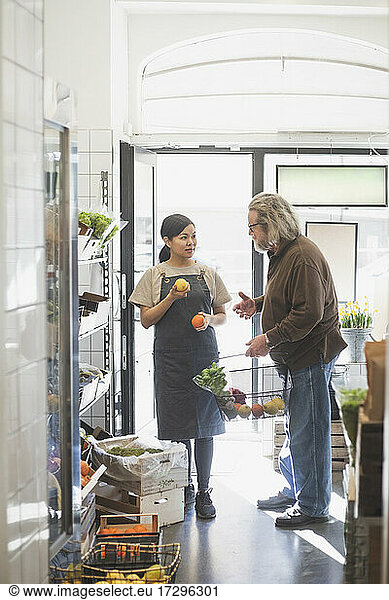Senior male customer talking with female owner while buying food in store