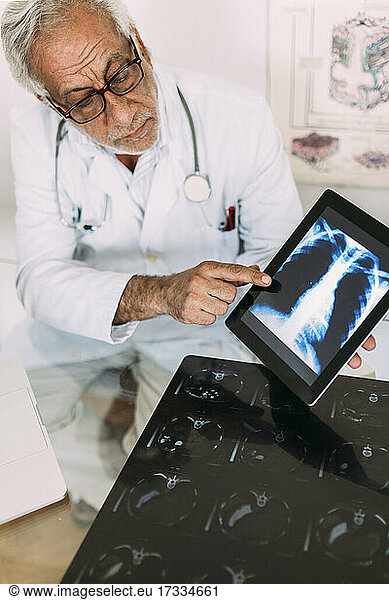 Senior male doctor explaining digital x-ray image on tablet in hospital