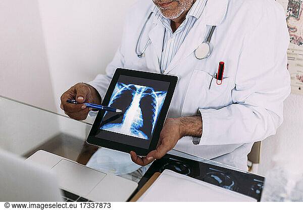 Senior male doctor explaining x-ray on digital tablet in hospital