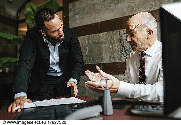 Senior male financial advisor discussing over contract with colleague at desk in office