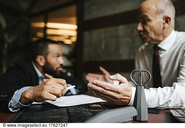 Senior male lawyer discussing over contract with colleague at desk in office