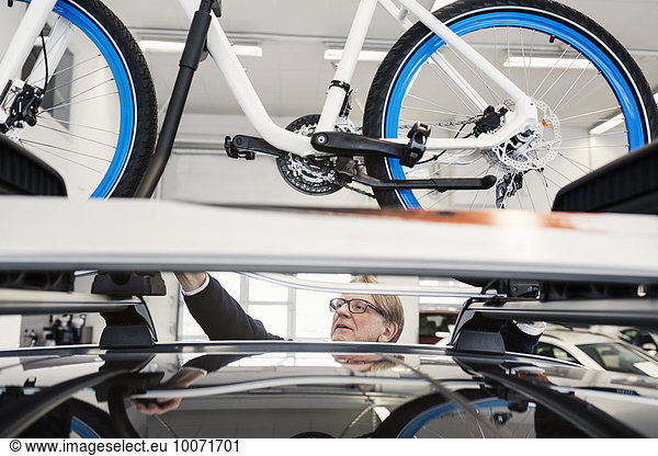 Senior man adjusting bicycle on car roof at showroom