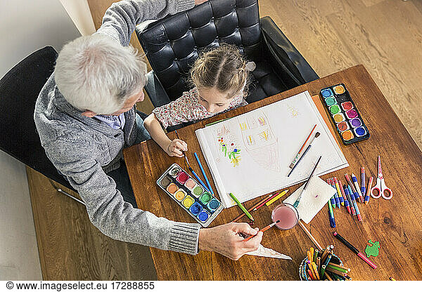 Senior man and girl painting in paper on table at home