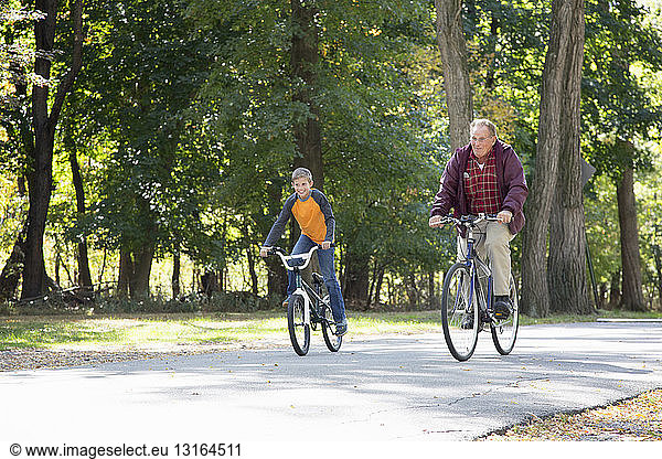 Senior man and grandson cycling through woods