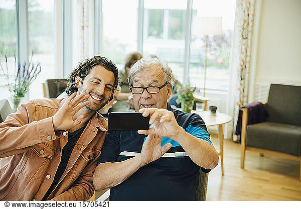 Senior man and grandson video conferencing on smart phone at elderly nursing home