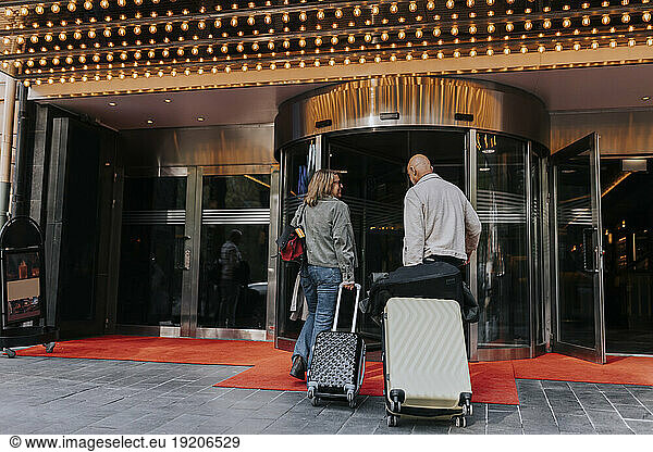 Senior man and woman puling luggage while entering in movie theater