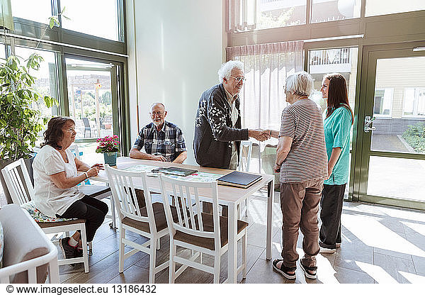 Senior man and woman shaking hands near friends and nurse at nursing home