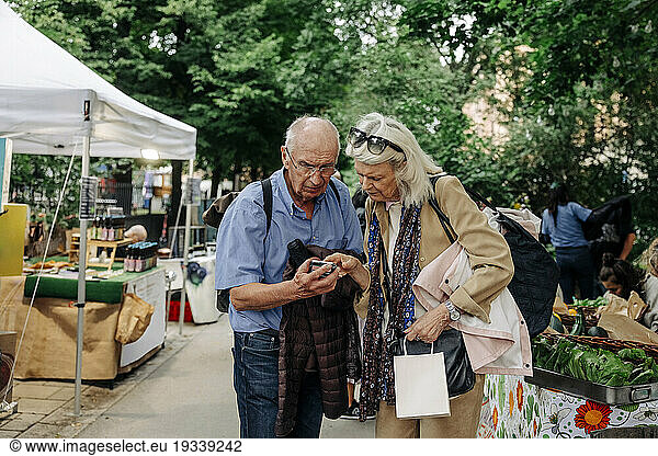 Senior man and woman using smart phone while standing at market place