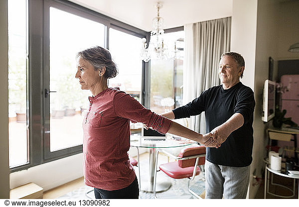 Senior man assisting woman in practicing yoga at home