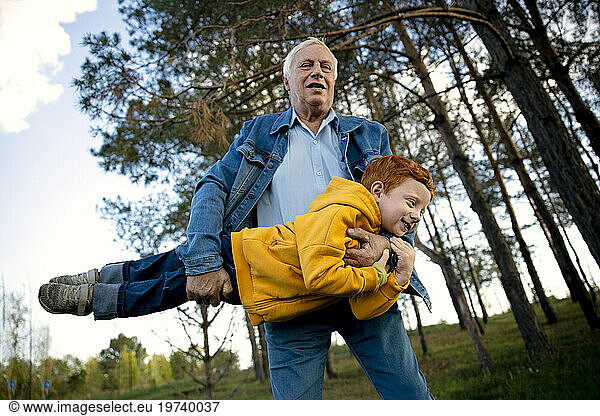 Senior man carrying grandson and playing in park