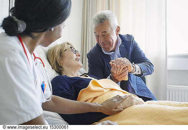 Senior man consoling female patient by doctor in hospital ward