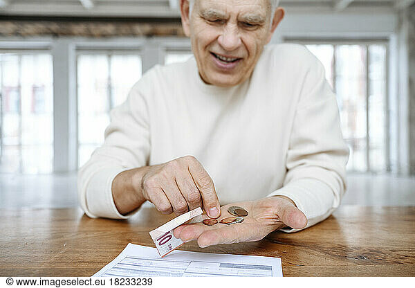Senior man counting coins on table at home