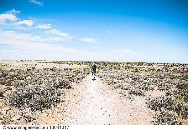 Senior man cycling on dirt trail against blue sky
