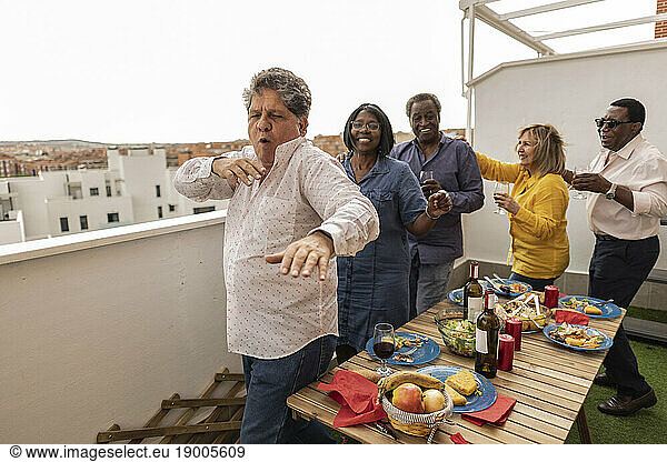 Senior man dancing with friends at dinner party in balcony