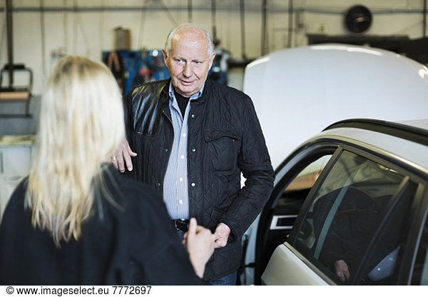 Senior man discussing with female mechanic at auto repair shop