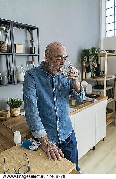 Senior man drinking water in kitchen at home