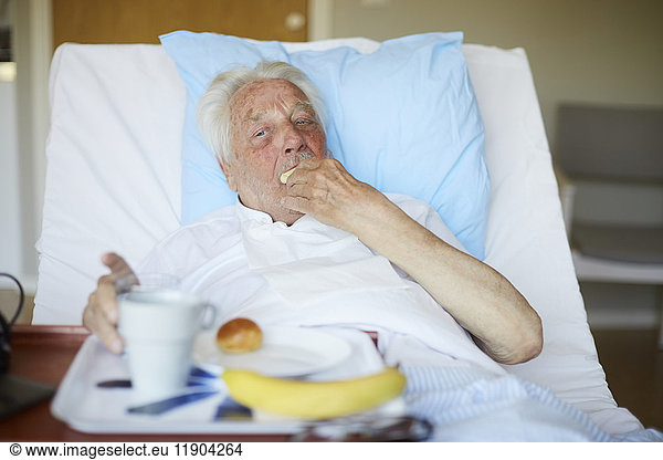 Senior man eating breakfast on bed in hospital ward