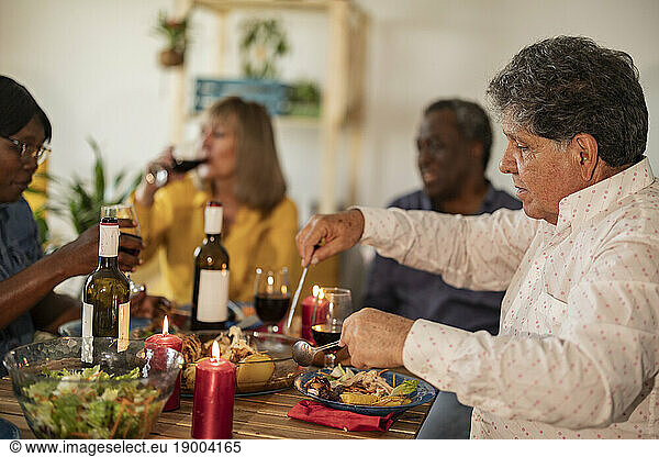 Senior man eating food with friends at dinner party