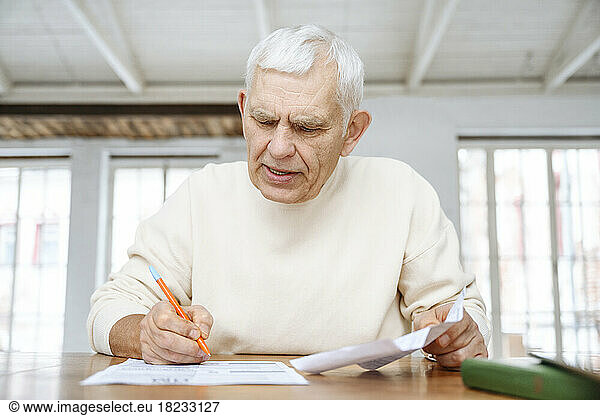 Senior man examining financial bills on table at home