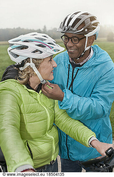 Senior man fastening on bicycle helmet to his wife and smiling  Bavaria  Germany