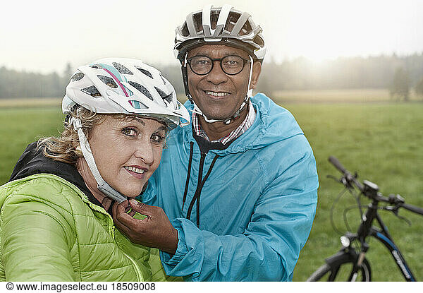 Senior man fastening on bicycle helmet to his wife and smiling  Bavaria  Germany