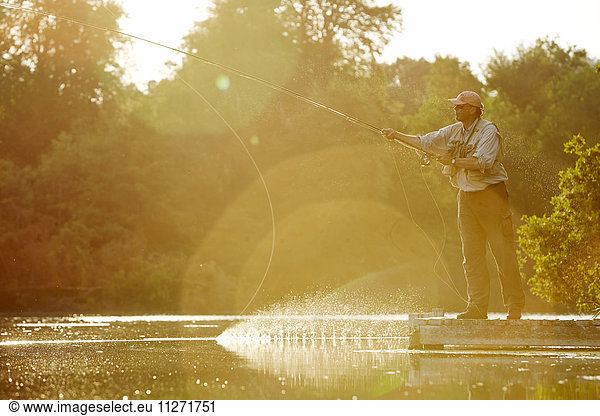 Senior man fly fishing at sunny summer lake