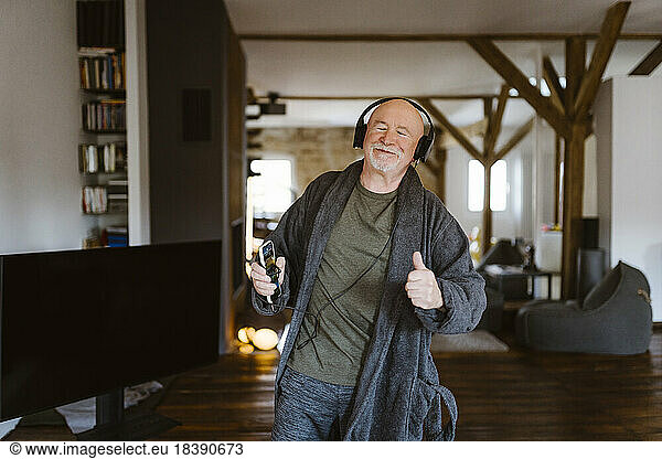 Senior man gesturing while enjoying listening to music through headphones at home