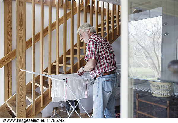 Senior man hanging clothes on drying rack while standing by wooden steps at home