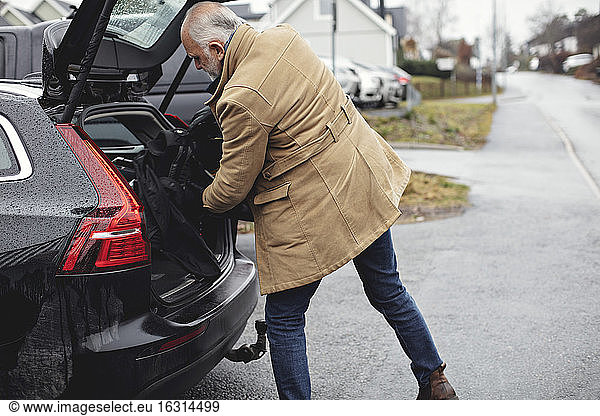 Senior man keeping golf bag in car trunk during winter