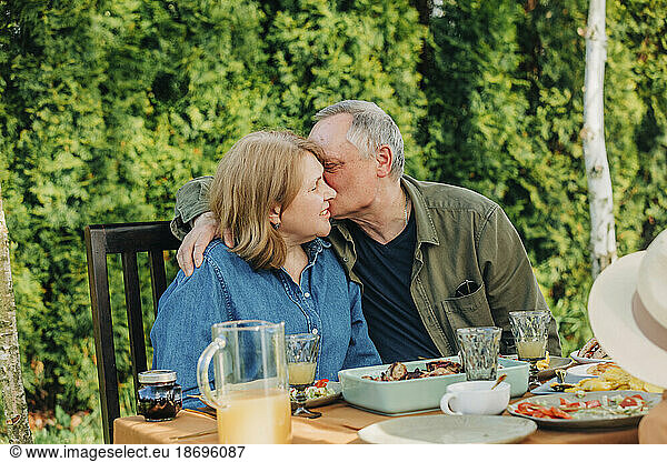 Senior man kissing woman sitting at dining table in back yard