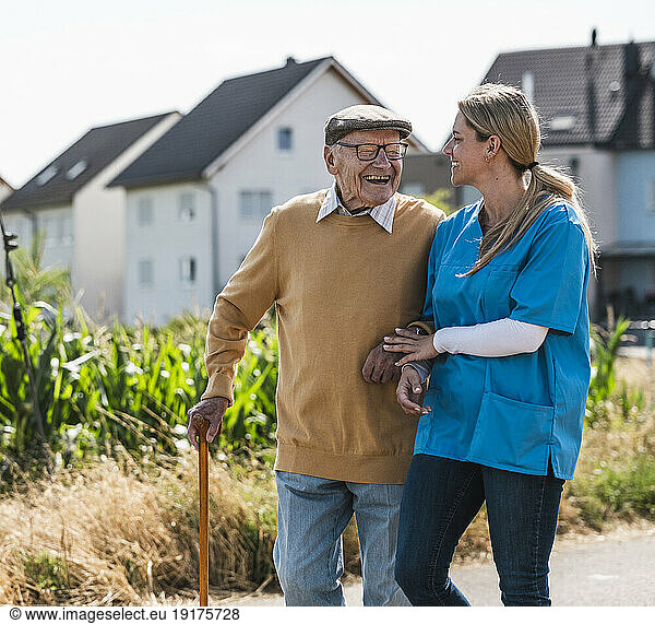 Senior man laughing and walking with nurse on sunny day