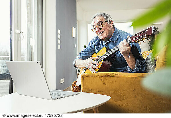 Senior man learning guitar through online tutorial on laptop at home