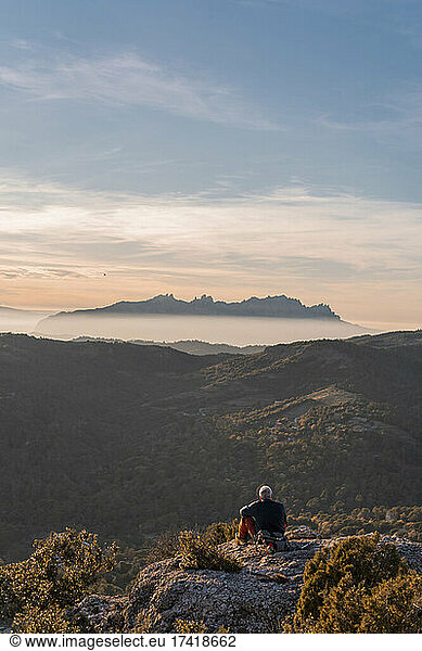 Senior man looking at mountain while sitting at cliff during hiking